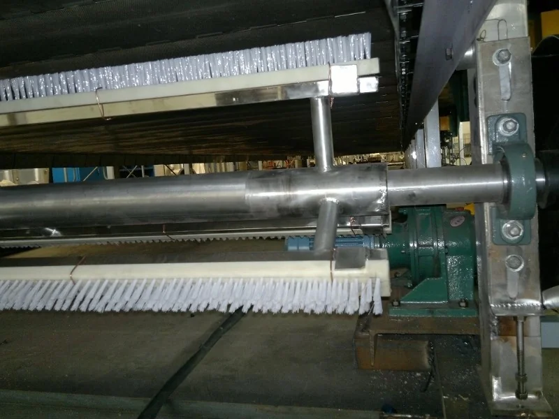 Brush mechanism for removing material from the dryer conveyor belt
