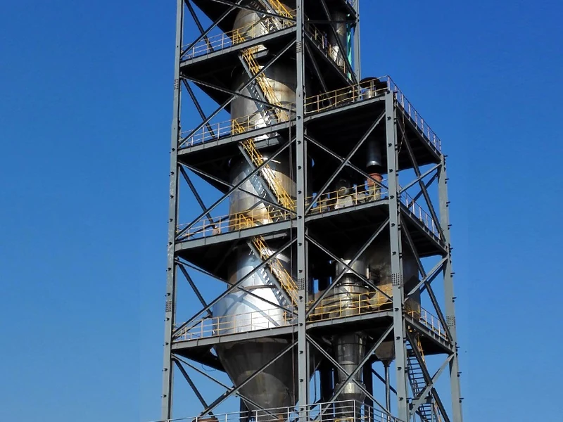 Tall dye spray drying tower within a steel support structure against a blue sky
